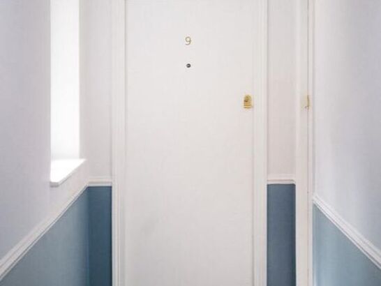 Apartment door at end of blue and white hall with the number 9 above the peephole.